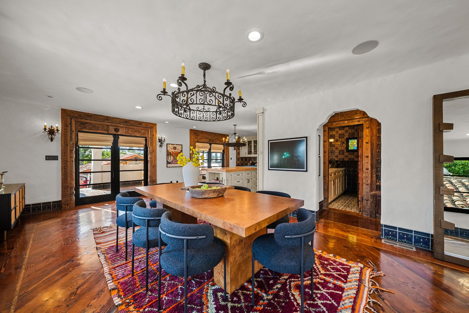 A wrought-iron chandelier hangs over a large wood table surrounded by eight blue upholstered chairs.