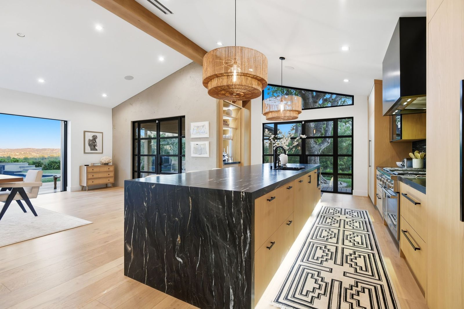 Kitchen with a long black stone island stretching through the middle of the room beneath two woven pendant lights.