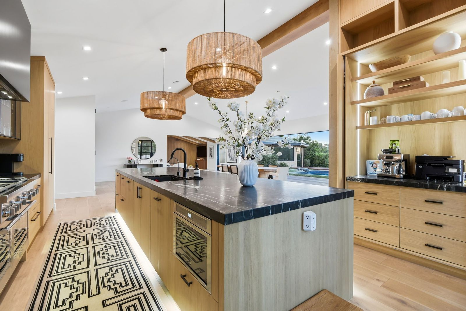 The island incorporates the sink, storage, and under-counter appliances, while a professional-style range and an illuminated built-in coffee station fill the rest of the space.