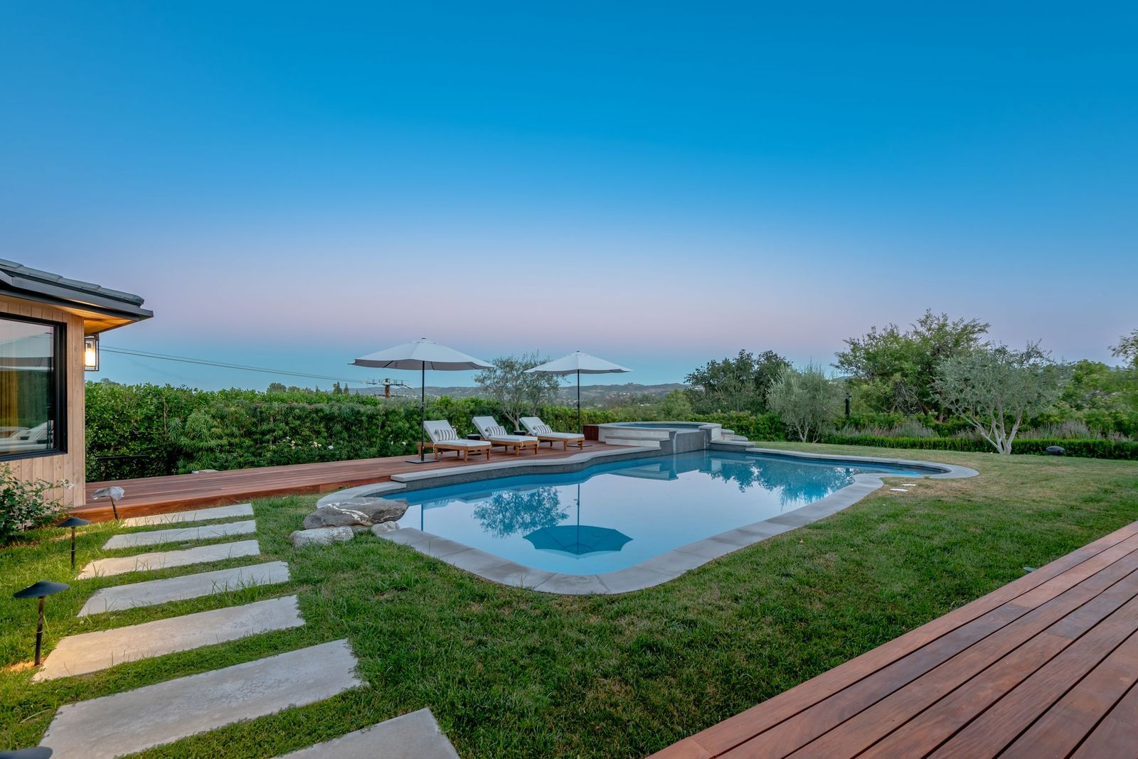 At the center of the space, a swimming pool curves around a raised spa, with lounge chairs and umbrellas arranged along the far edge to preserve open hillside views.