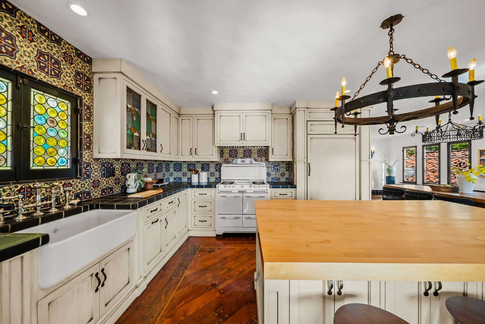 A farmhouse sink is positioned beneath stained-glass windows and the original vintage stove sits alongside integrated Sub-Zero refrigeration. 