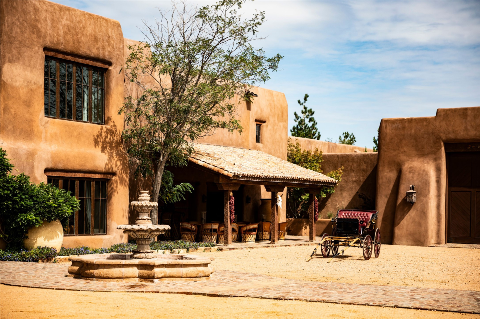 Across the plaza, the coach house is set behind a courtyard with a stone fountain, shaded portico, and room for horse-drawn carriages. 
