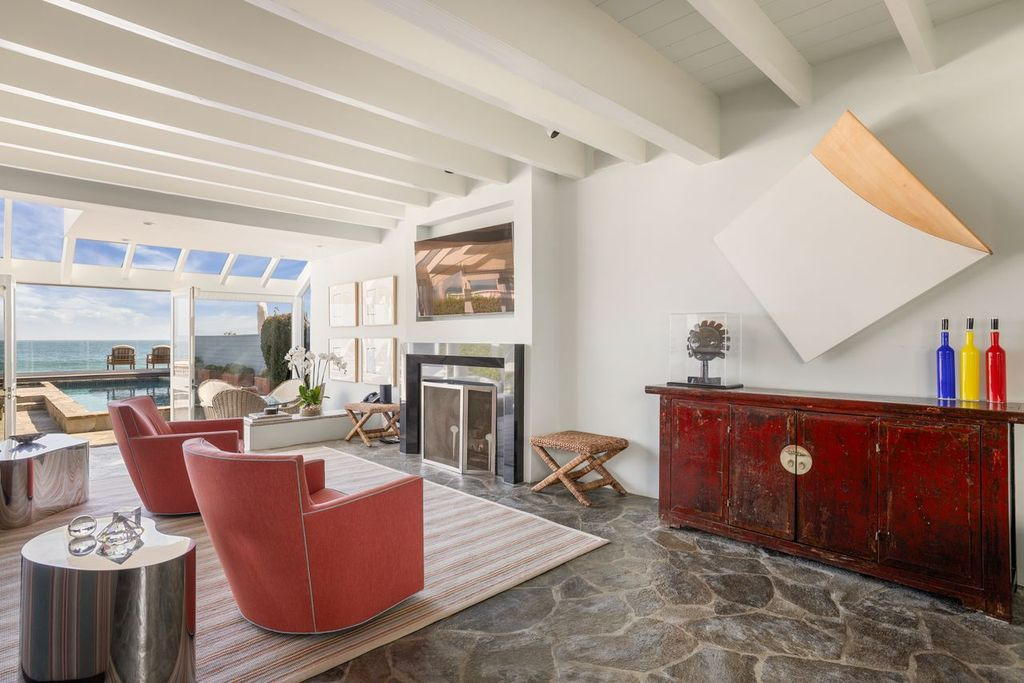 Stone flooring runs through the room toward a wall of glass doors, where the interior opens directly onto the beachfront terrace and pool. 