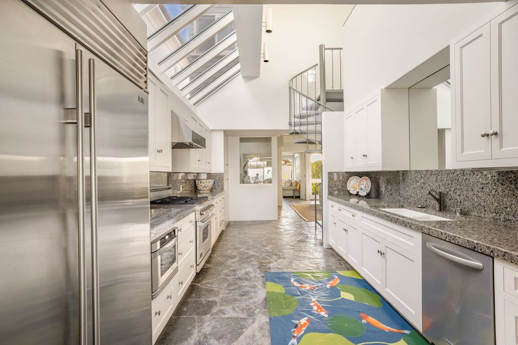 At the center of the main house’s lower level is a kitchen, with white cabinetry and speckled stone counters running along both sides of the narrow space. 