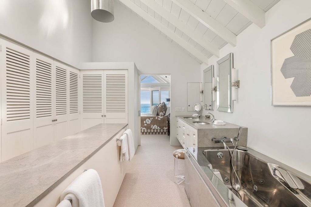 The en-suite bathroom has a long vertical layout with a double vanity and a stainless-steel jetted soaking tub sitting next to each other against the right wall.