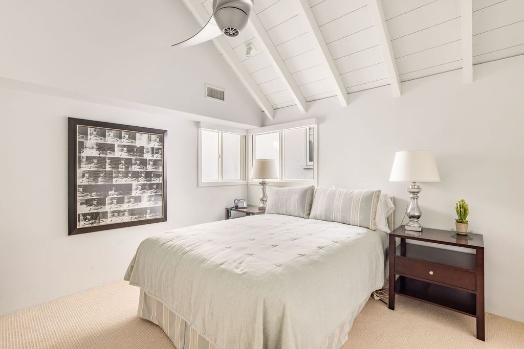 Bedroom with a bed that sits low against the inner wall between two dark wood nightstands and a framed black-and-white artwork.