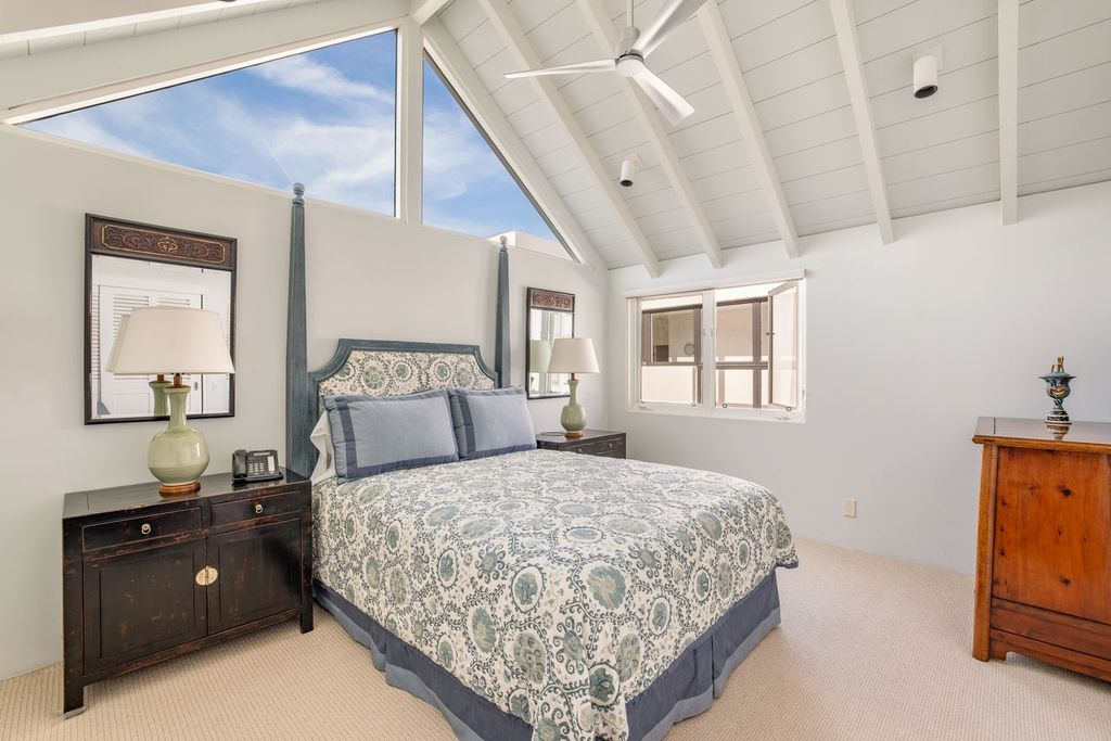 A carved four-poster frame and patterned bedding bring contrast to the otherwise pale room, while matching dark nightstands sit against the white walls.
