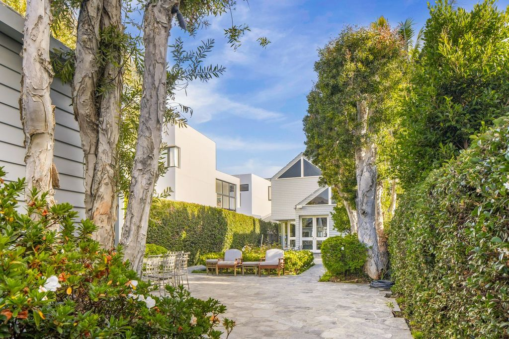 Tall trees, clipped hedges, and built-in planting beds line the walkway, while a small dining and seating area occupies the center between the two buildings.
