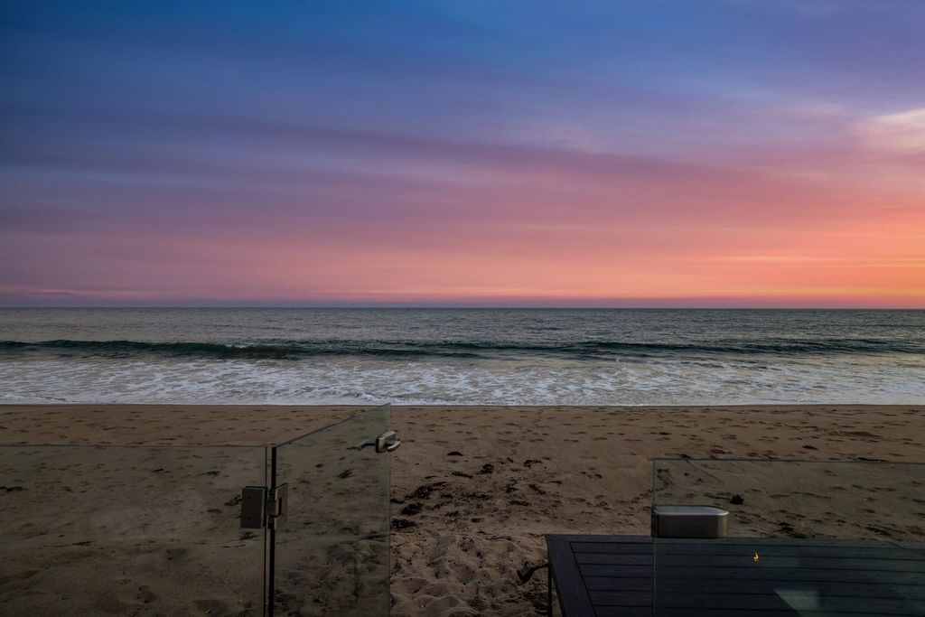 A glass railing opens directly to the sandy beach.