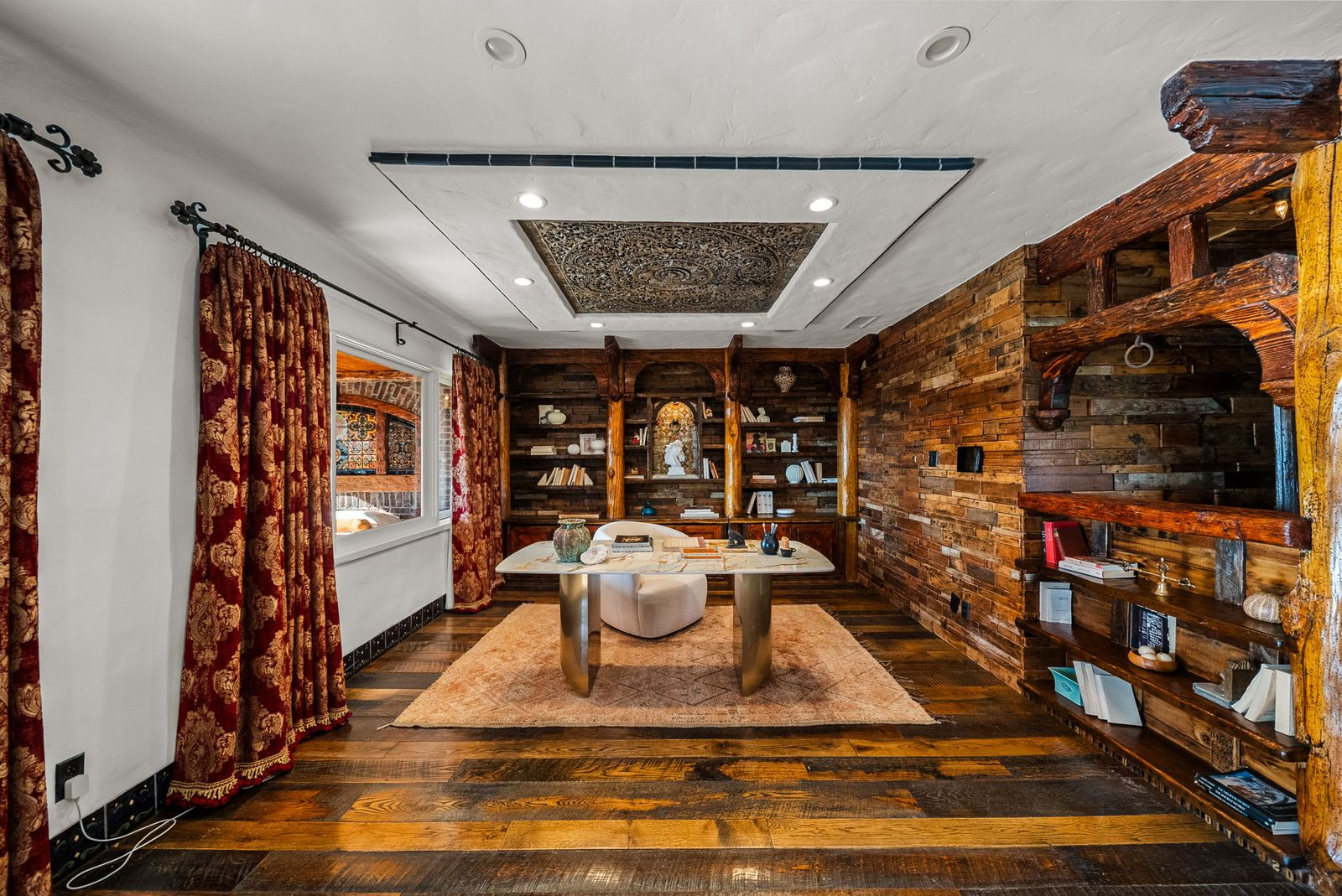 Right around the corner, the office continues the same warm palette with reclaimed wood walls, custom built-in bookcases, and a carved ceiling medallion above the workspace.