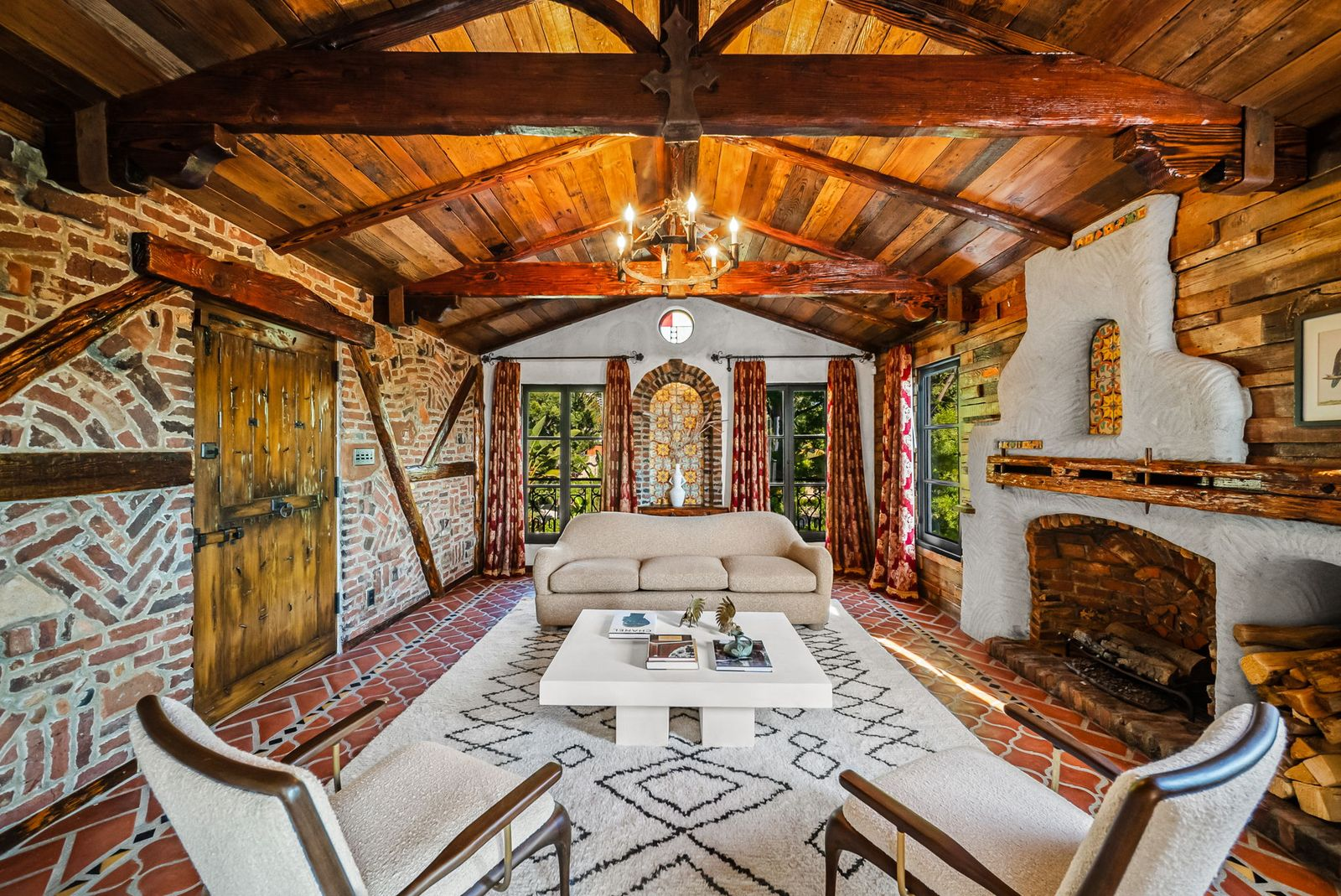 The den is defined by a vaulted wood-plank ceiling with exposed timber trusses, a traditional adobe-style fireplace, and brick walls surrounding an antique wooden door. 
Family