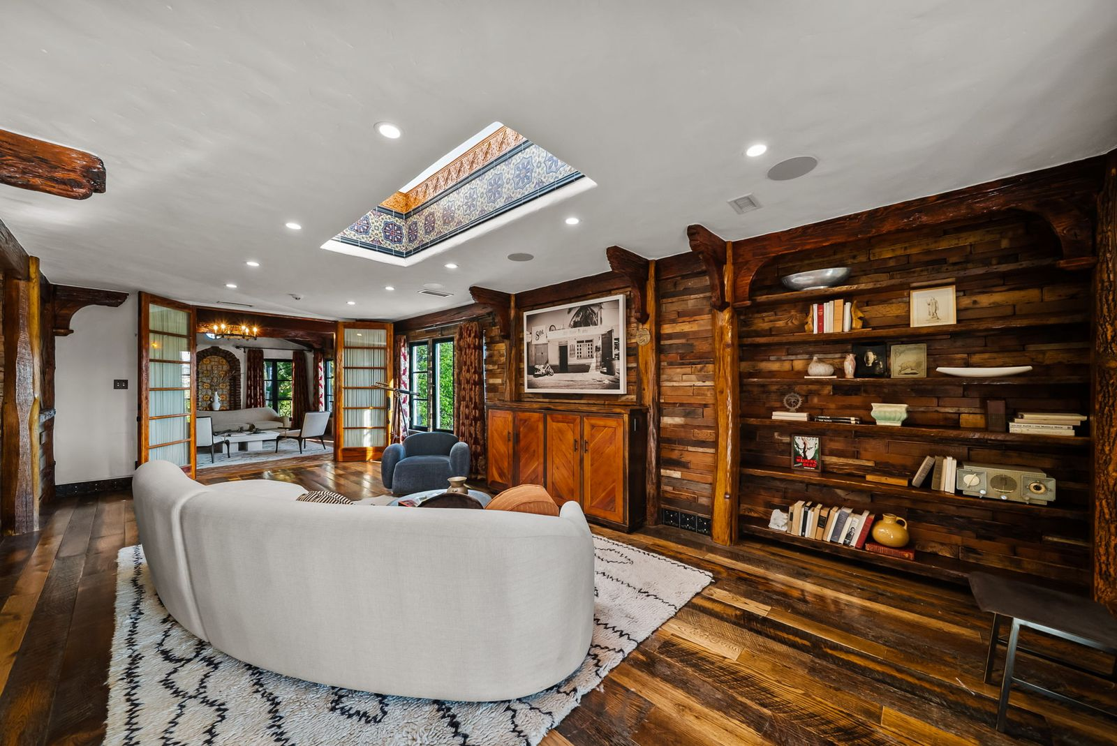 Just beyond, the den introduces darker reclaimed wood flooring, built-in shelving, and a decorative skylight framed by colorful Moroccan tile that fills the space with natural light.
