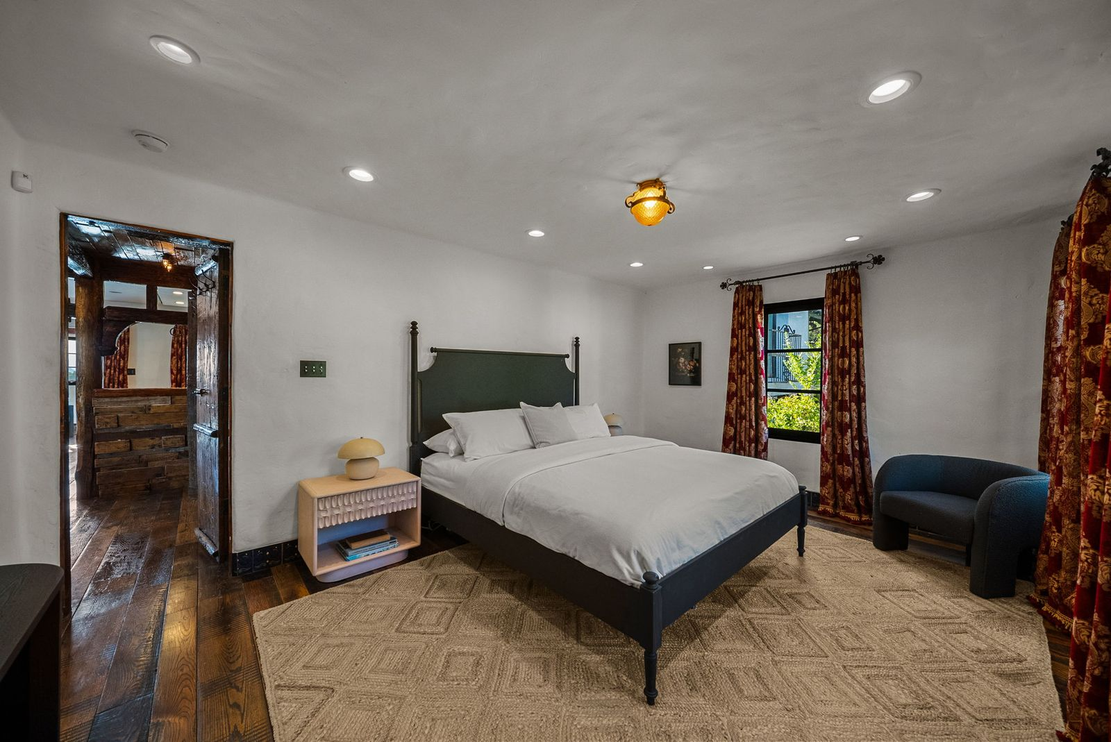 The second guest bedroom offers a simpler design with dark hardwood floors, smooth plaster walls, and black-framed windows overlooking the surrounding greenery.