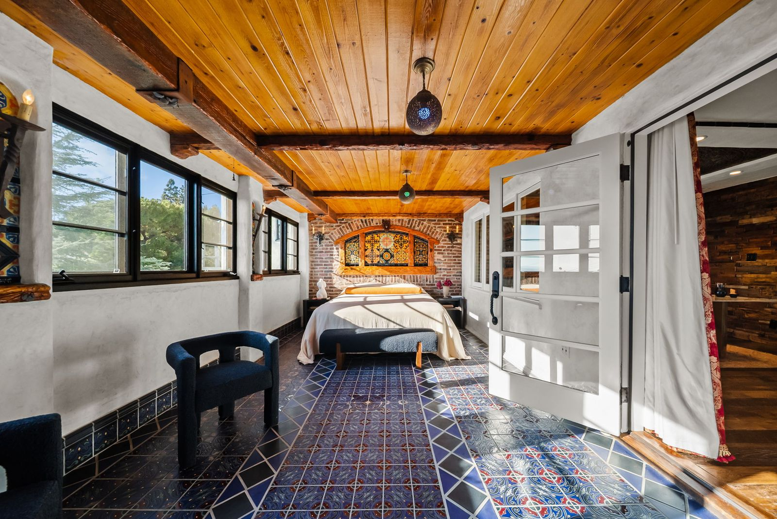 Bedroom with exposed timber ceilings, brick walls, and intricate Moroccan tile flooring. 