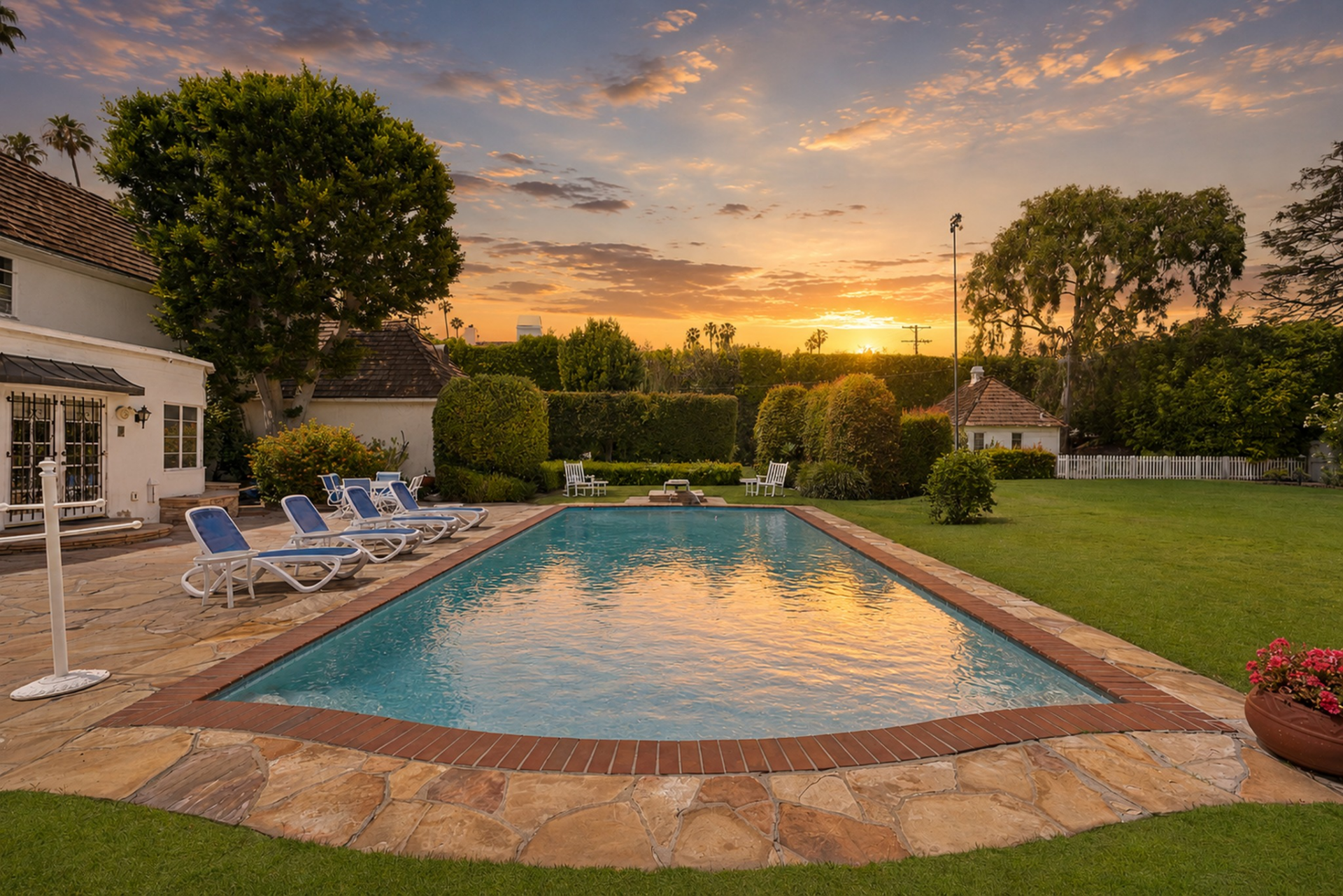 The long rectangular swimming pool, bordered by a wide stone patio lined with lounge chairs and a diving board at the far side.