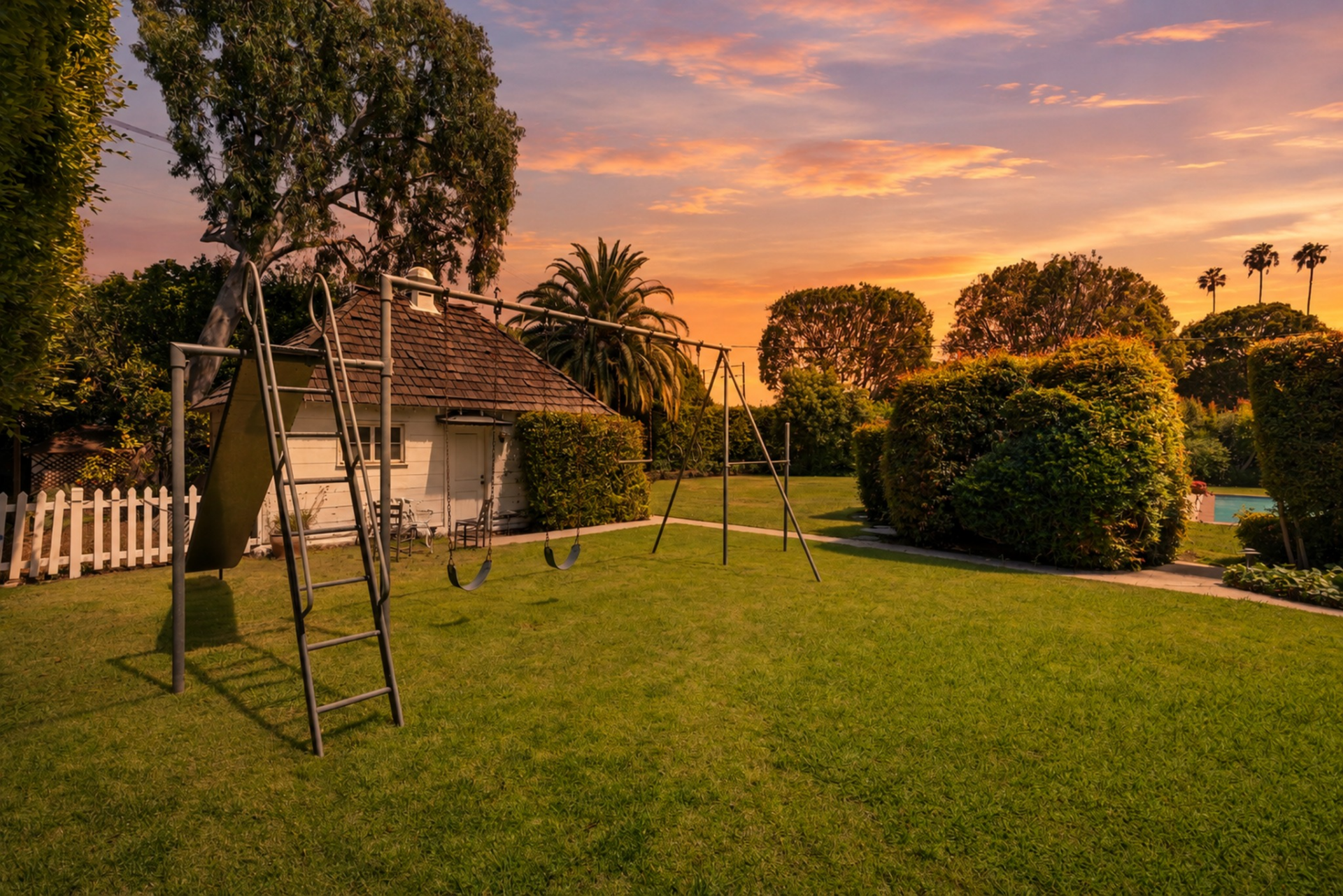 Set on its own section of lawn past the pool, the playground includes a swing set and slide positioned beside a small outbuilding with a cedar shake roof. 