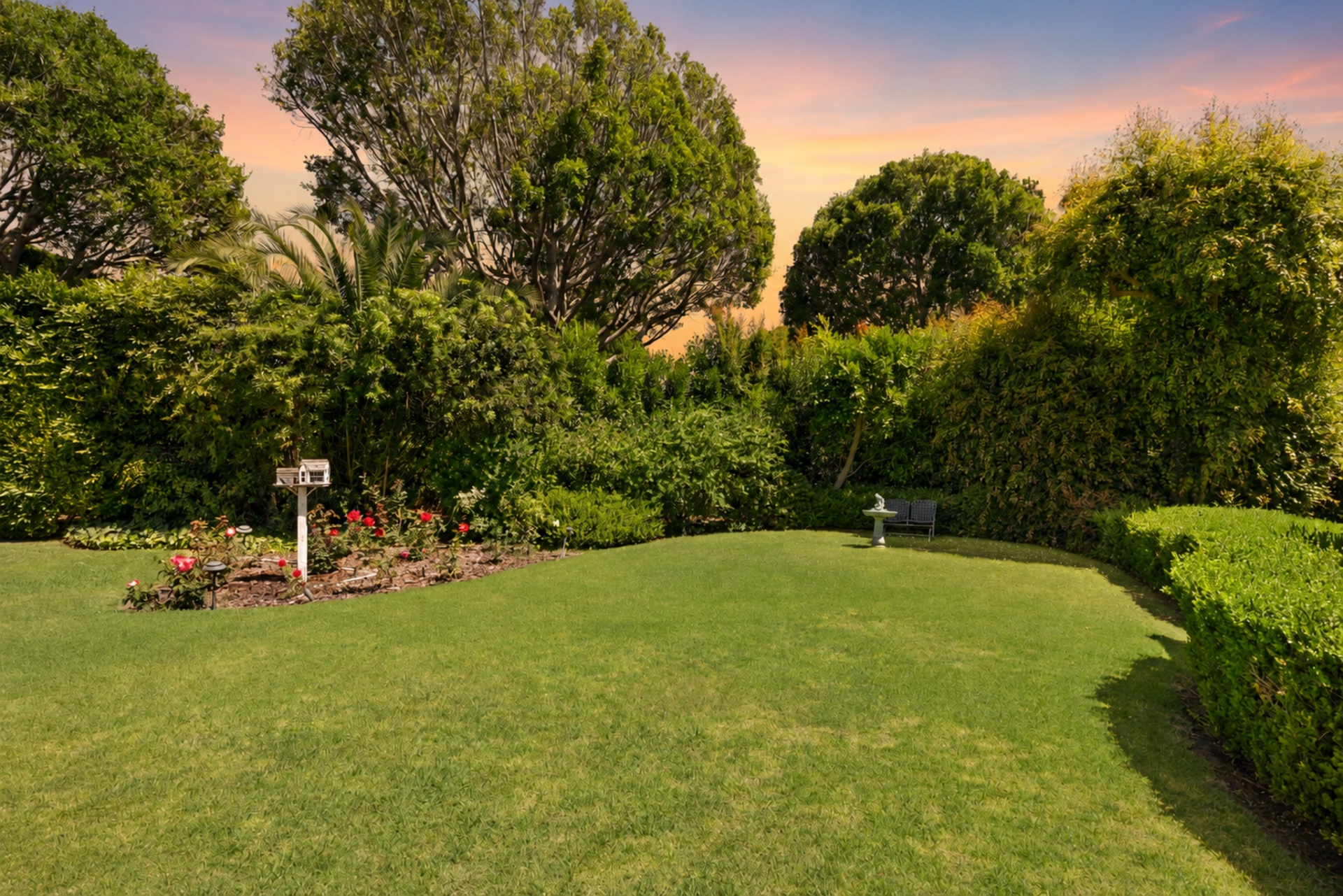 The lawn past the pool extends into a garden framed by trimmed box hedges, flowering beds, and mature landscaping.
