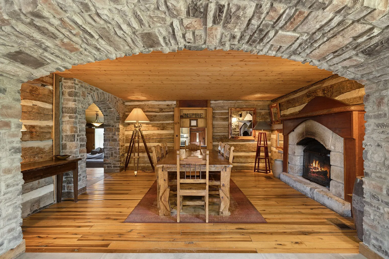 A dining room where exposed hand-hewn timber walls, wide-plank hardwood floors, and a stone fireplace.