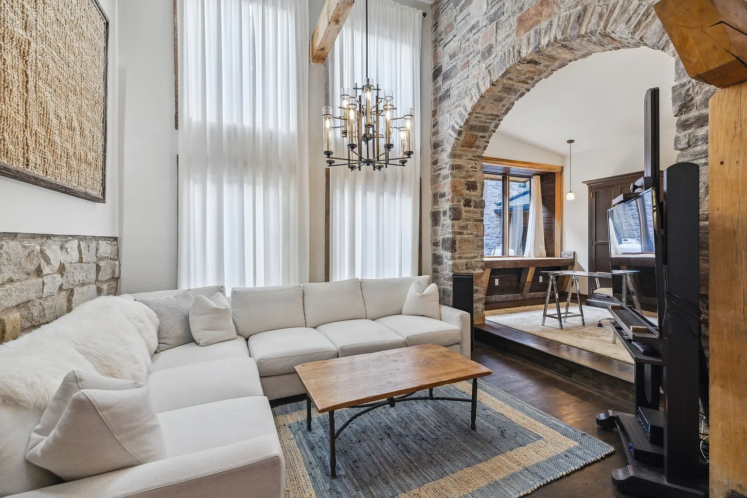 Natural light fills the living room through double-height windows dressed with floor-to-ceiling curtains.
