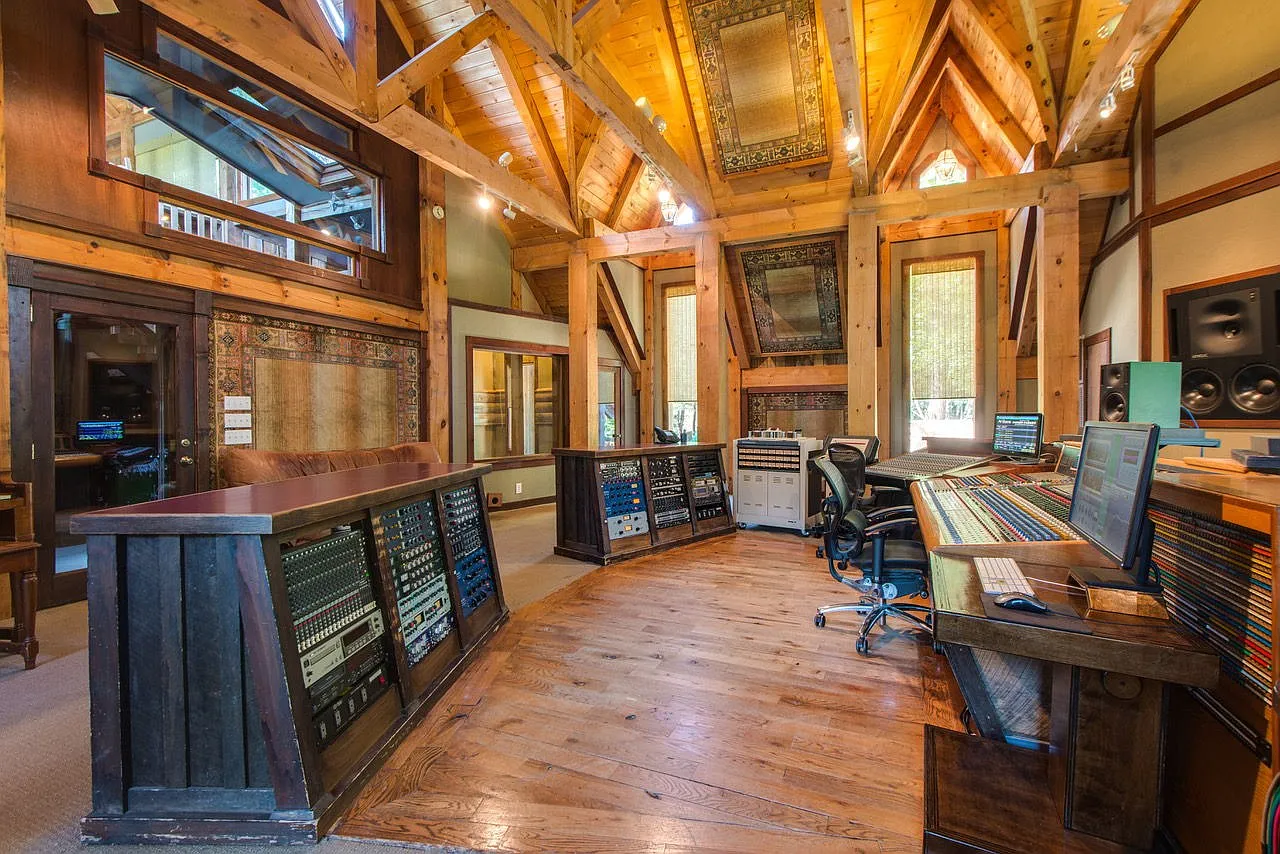 Exposed timber trusses soar overhead, while expansive control surfaces, rack-mounted analog equipment, studio monitors, and custom acoustic treatments.