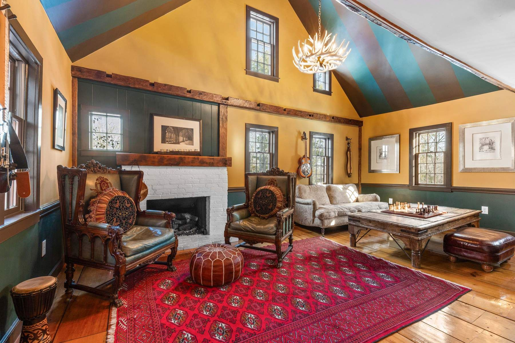A warm, double-height living room where the original wide-plank floors, exposed hand-hewn beams, and striped vaulted ceiling draw the eye upward.