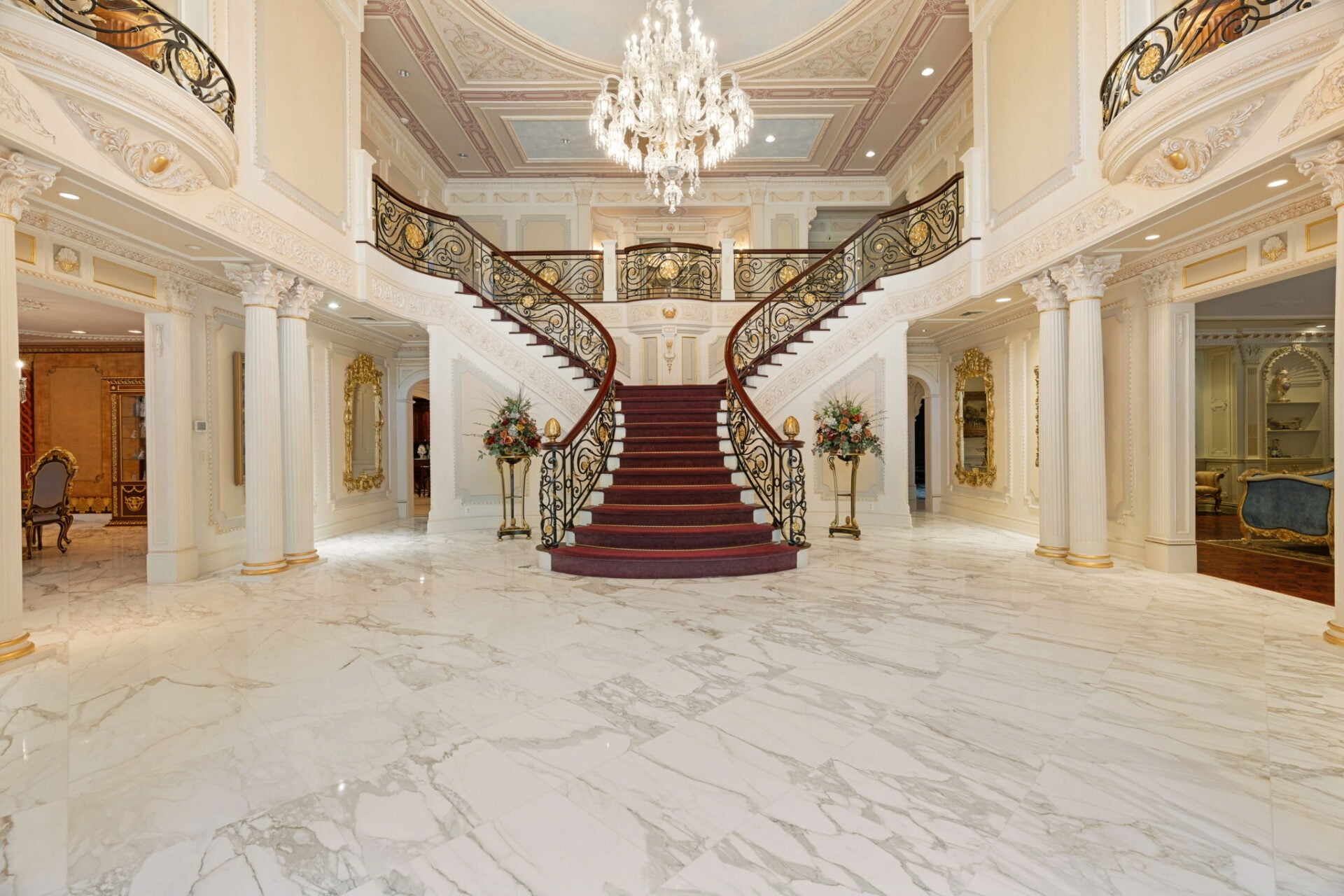 A split staircase rises from the center of the room, curving toward the upper galleries set behind wrought-iron railings with gold accents.