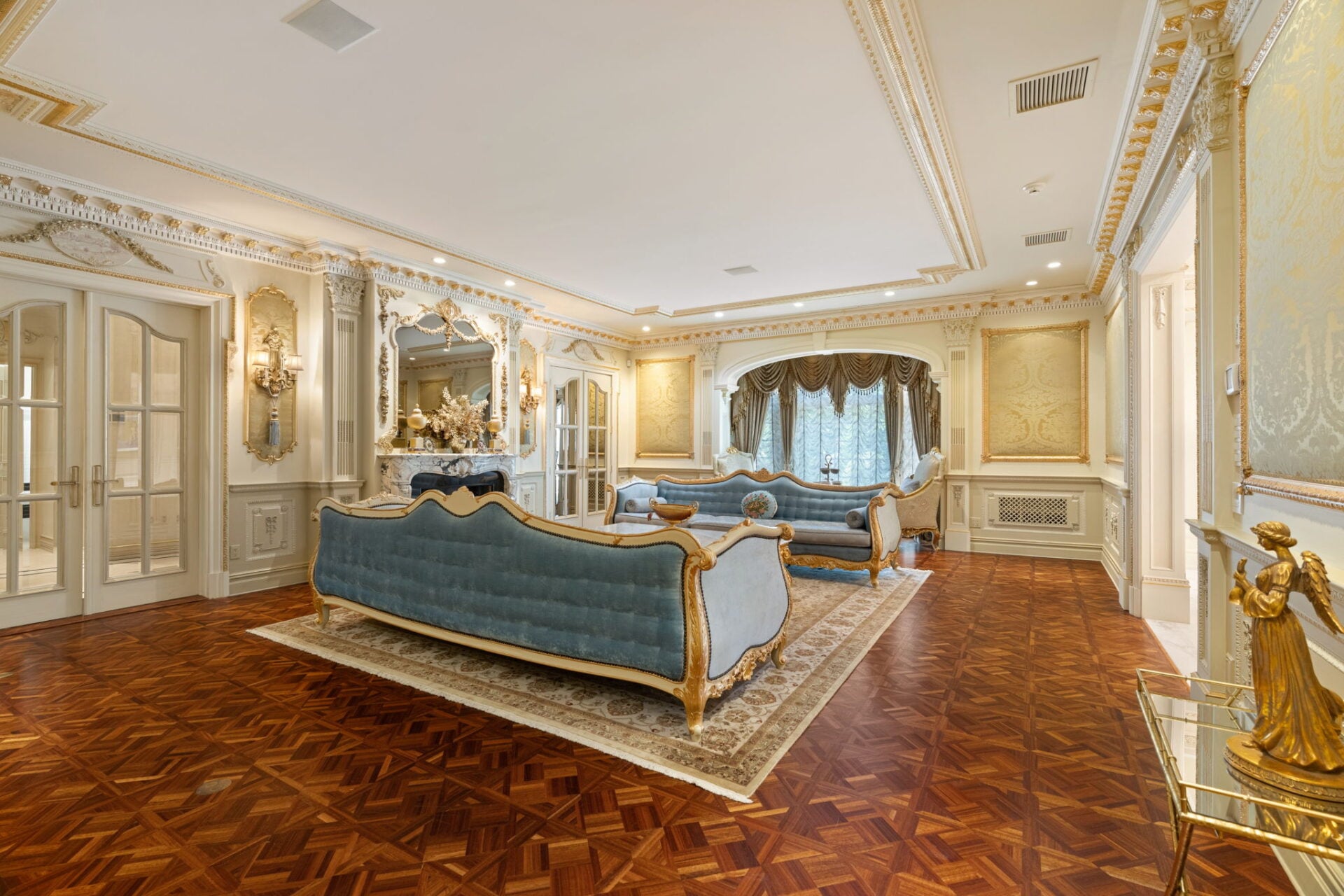 Blue velvet couches lined in gold trim placed to frame a carved marble fireplace beneath a decorative mirror.