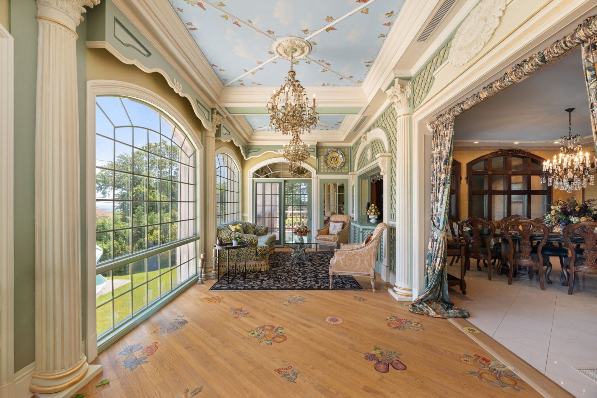 Towering arched windows line the exterior wall, while fluted columns, lattice-patterned panels, and soft green accents give the room a highly decorative, European-inspired design.