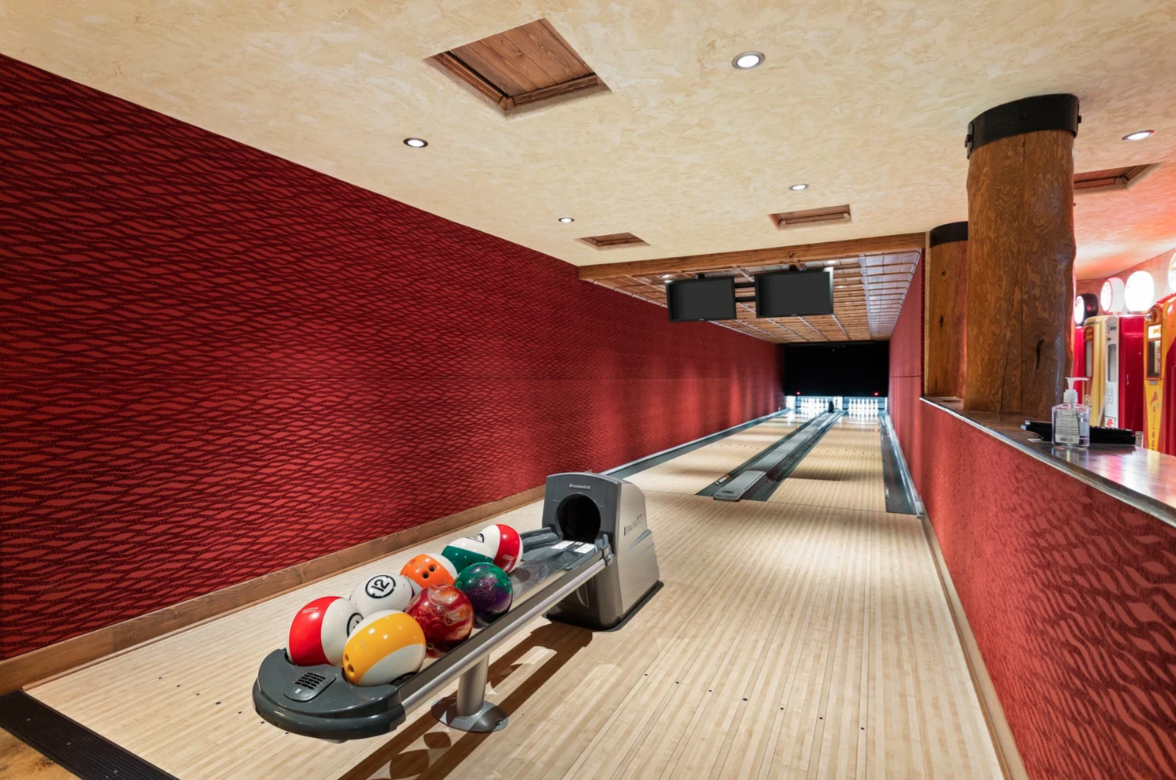Right past the lounge, the room narrows into a private two-lane bowling alley finished with deep red walls, overhead scoring monitors, and its own ball return at the head of the lanes.