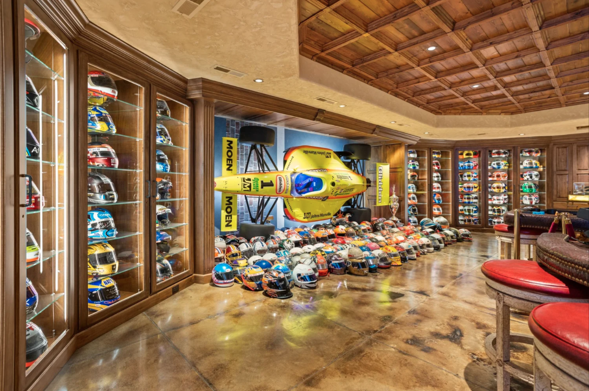 Behind the gaming tables, racing memorabilia with illuminated display cabinets wraps the walls, holding rows of helmets, while a full race car is mounted in the center of the wall.