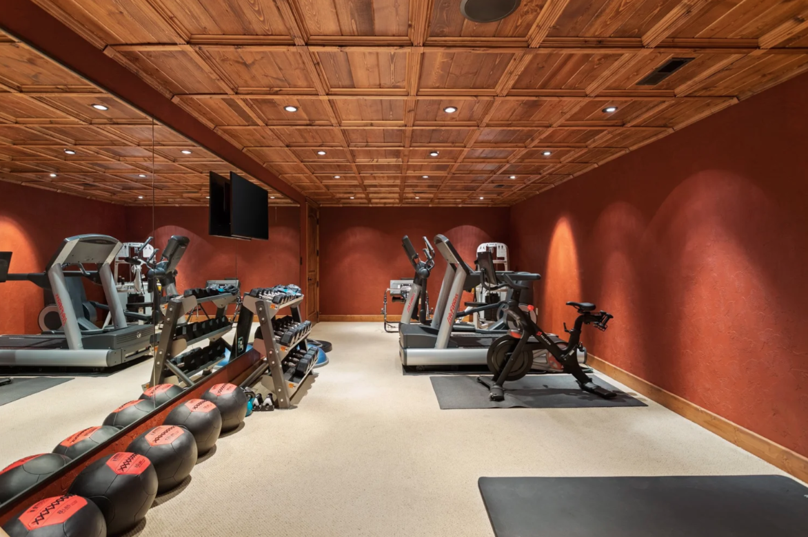 The lower level finishes with a private gym, where a mirrored wall runs beside rows of cardio and strength equipment.