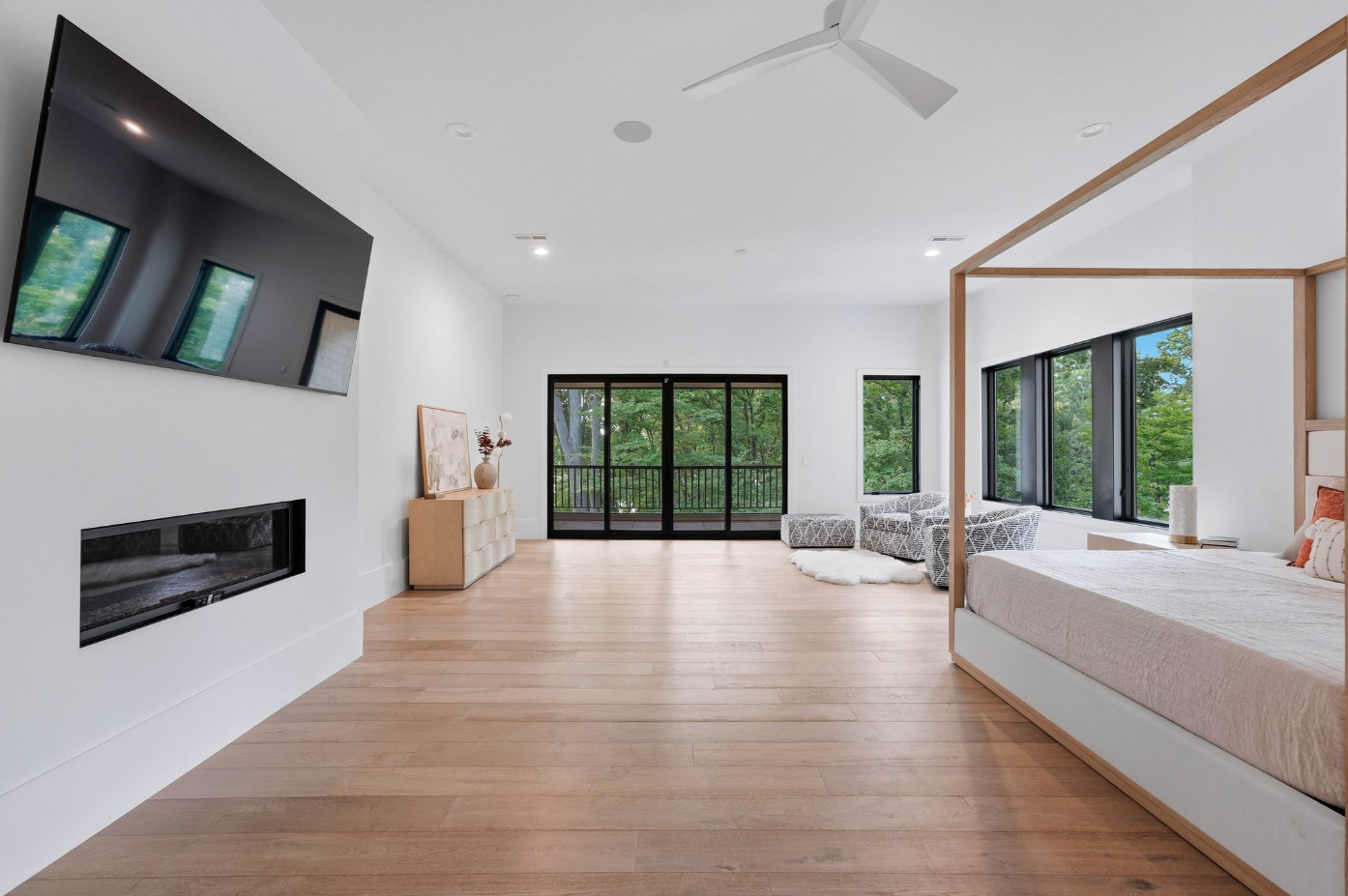 The bedroom stretches across pale French oak flooring with a four-poster bed positioned across from a linear fireplace and television. 