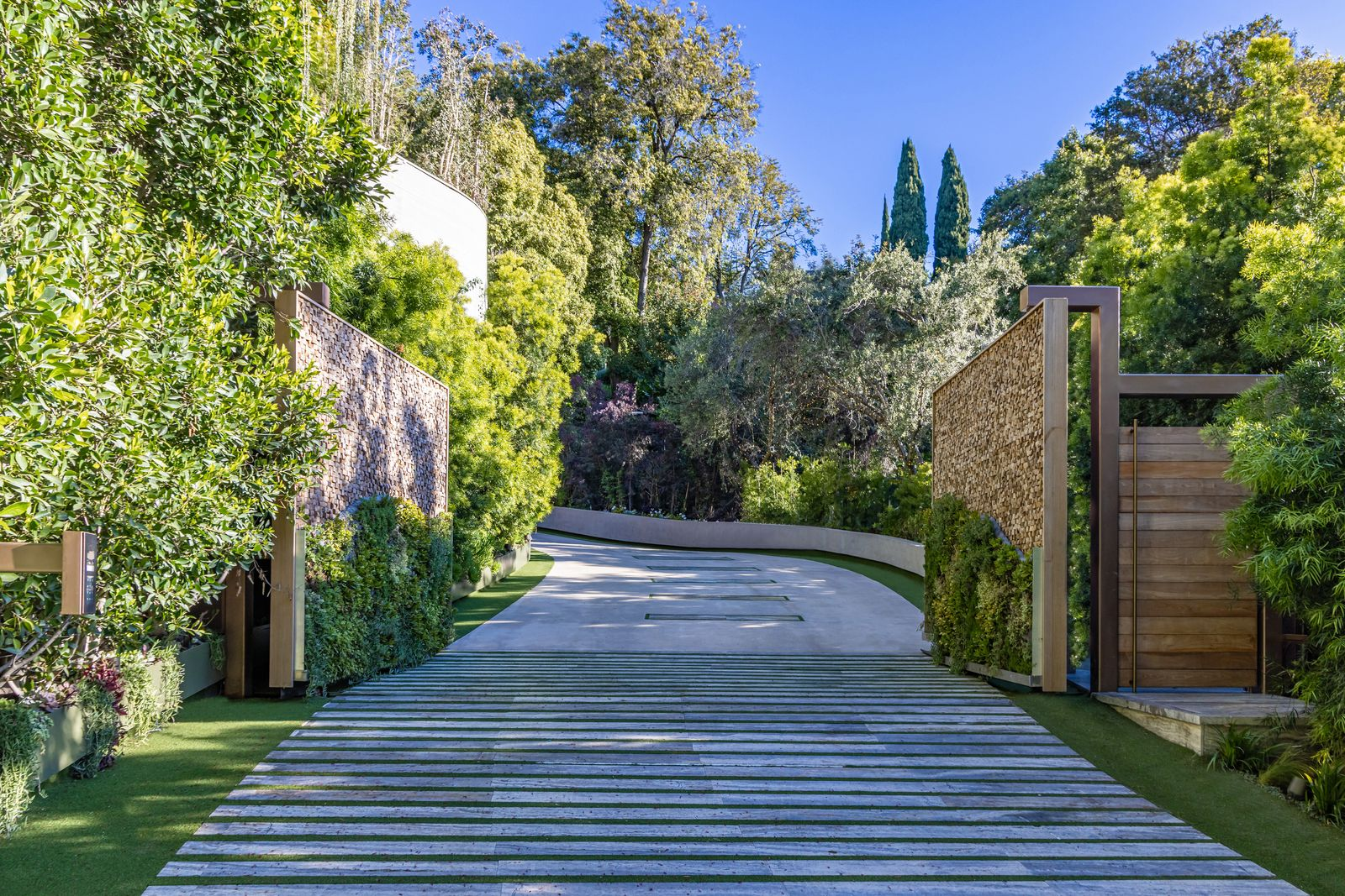 A wide driveway curves through dense landscaping before arriving at the front of the home.