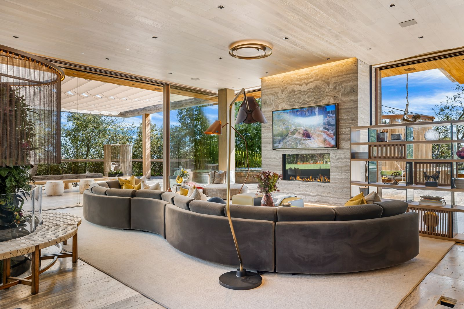 A few steps away, the media room shifts into a lower, more intimate setting organized around a stone fireplace beneath a mounted TV.