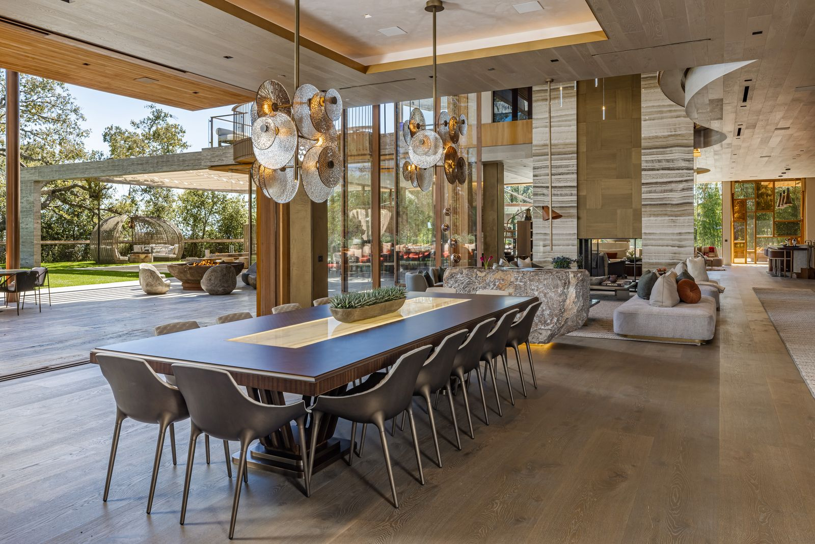 Just behind the open living room, the dining area continues the same expansive main-floor layout, with a long rectangular table positioned beneath two sculptural pendant lights.
