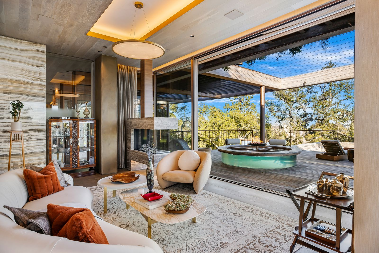 Curved seating faces the fire, while the room opens directly to the patio, where a circular outdoor fire feature sits beneath the open canopy.
