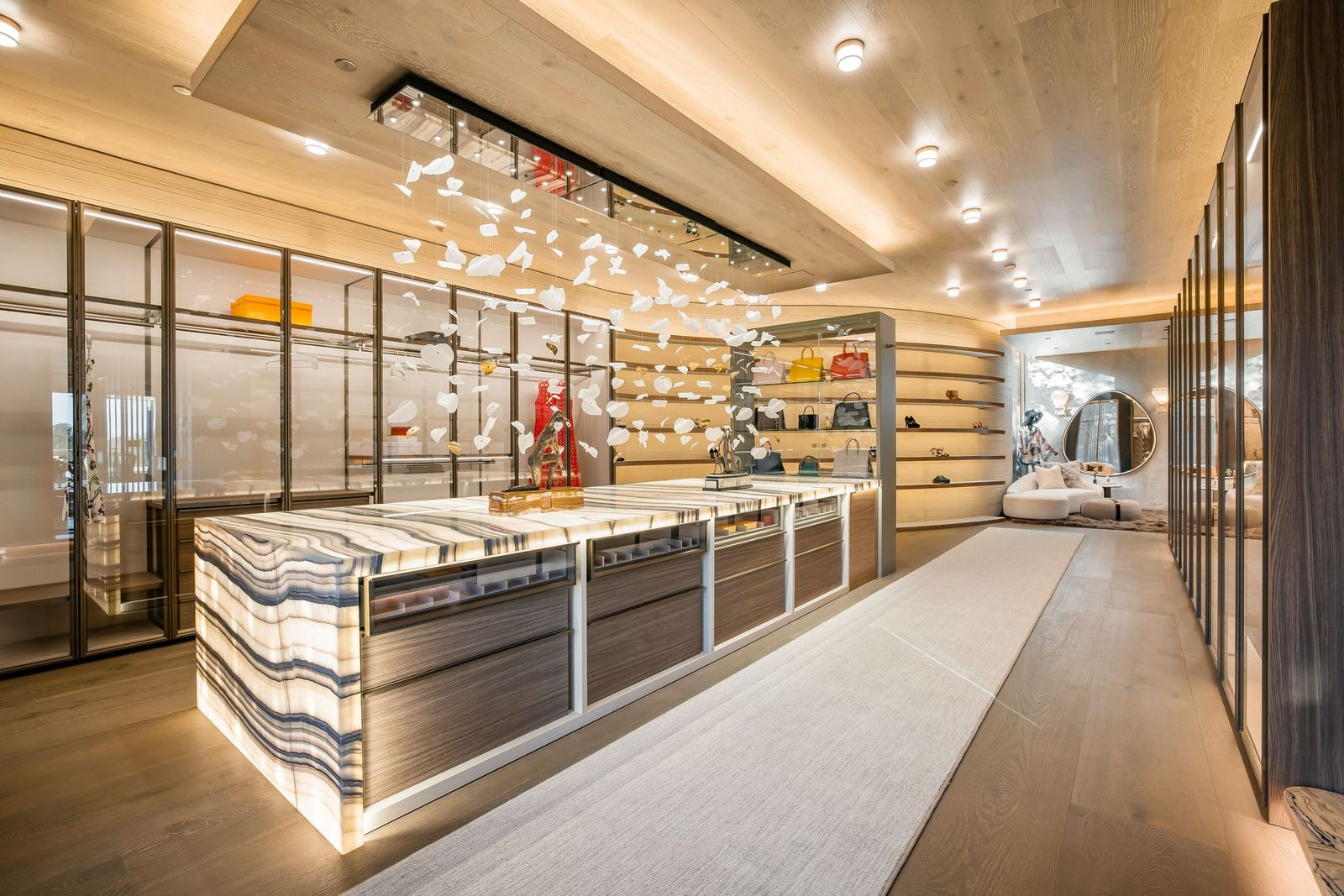 Glass-front wardrobes line both sides, with illuminated shelving, drawers, and display areas built into the wood-paneled walls.