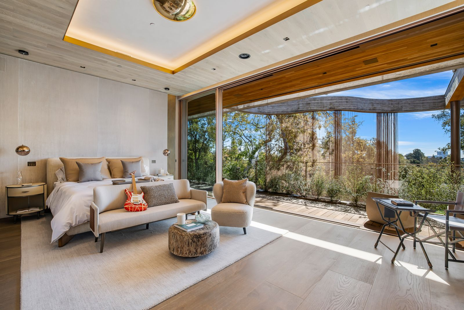 The second bedroom looks almost exactly like the previous one, with the bed set to one side and a small seating and work area positioned closer to the glass.
