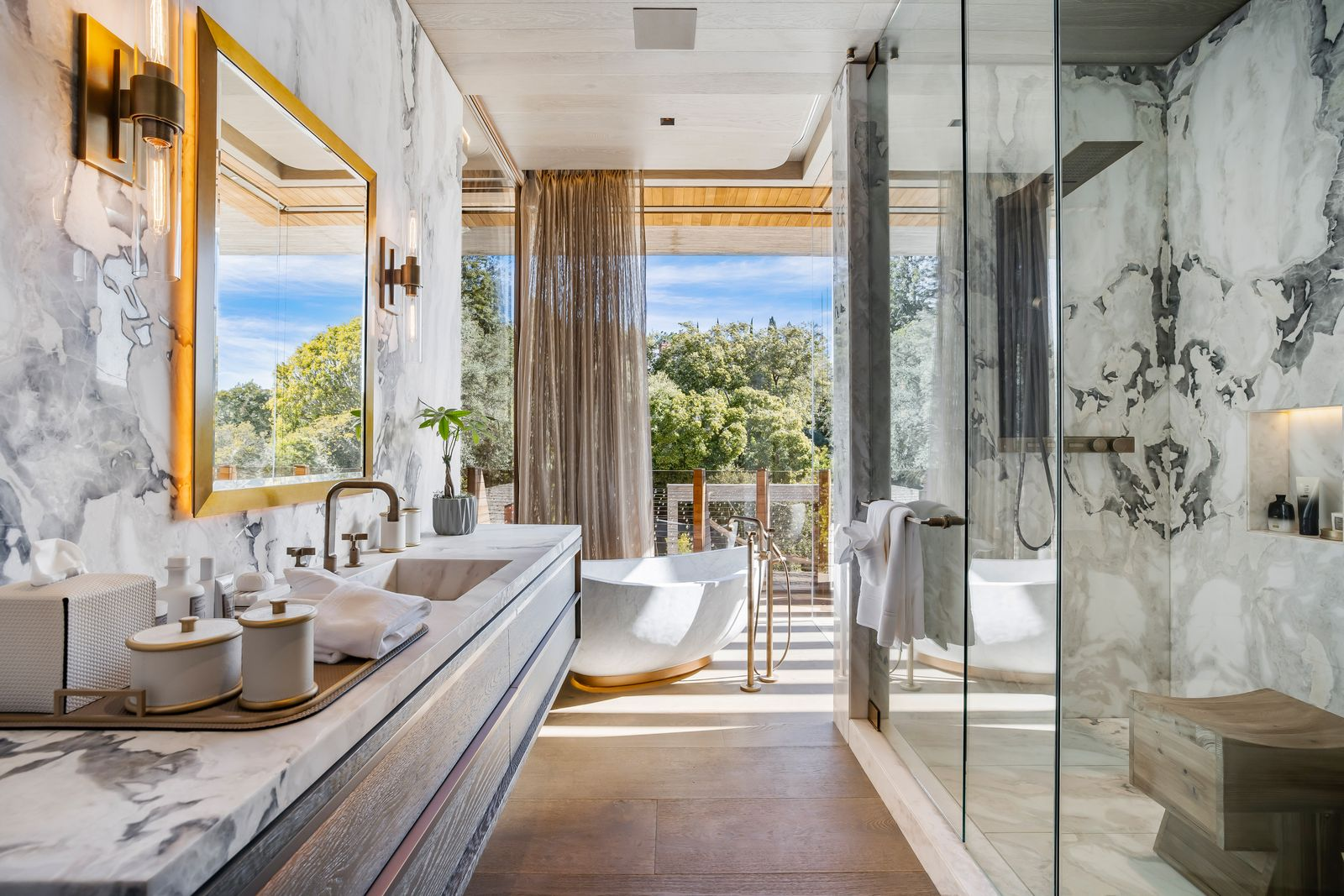 Linear bathroom with a long vanity running along one wall and a freestanding tub placed at the far end beside the windows.