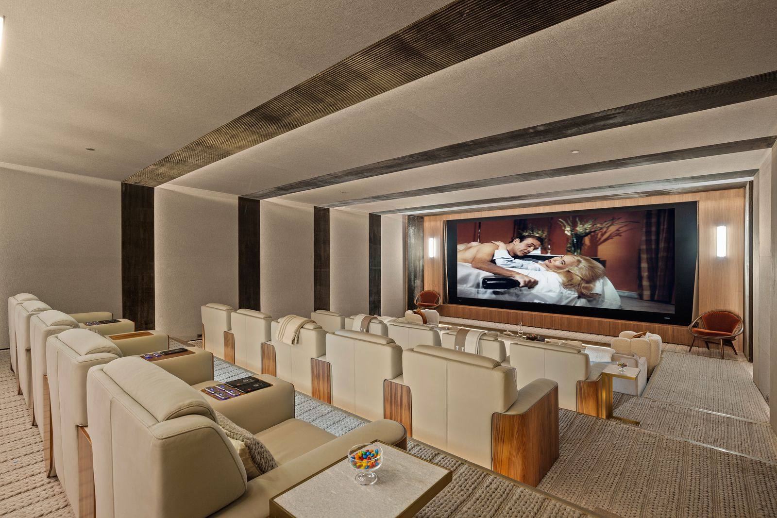 The screening room shifts features multiple rows of oversized cream-colored recliners descending toward a large projection screen.