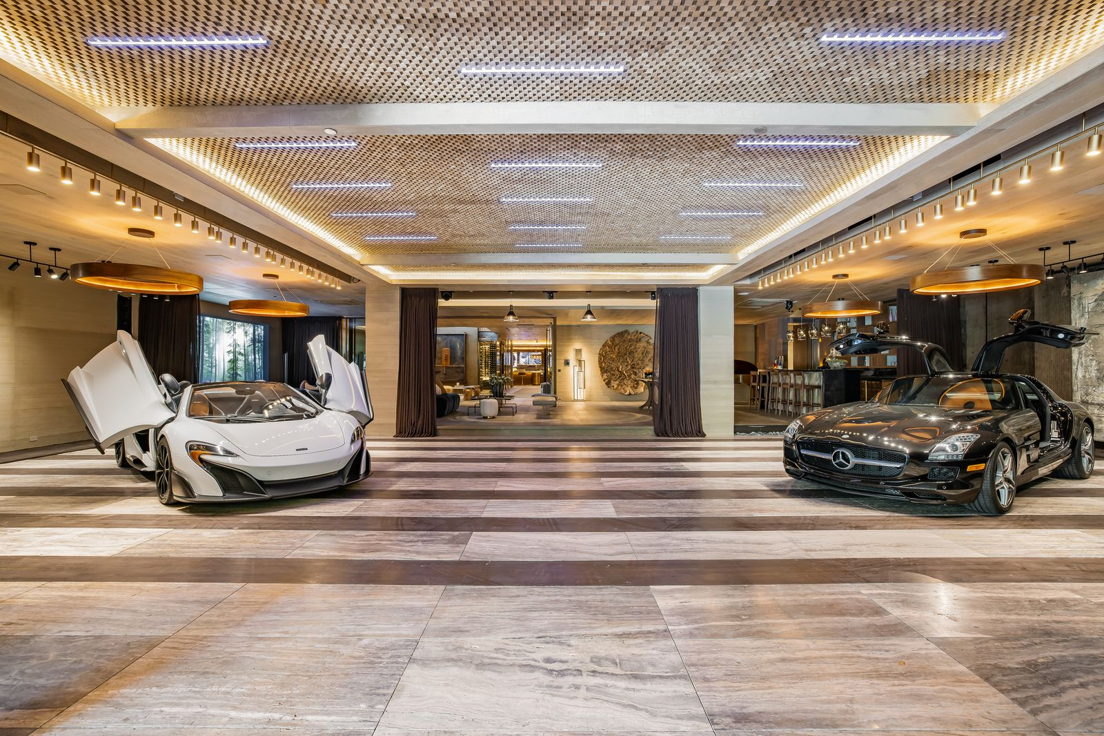 A six-car auto gallery where cars are displayed across polished stone floors beneath a geometric illuminated ceiling.