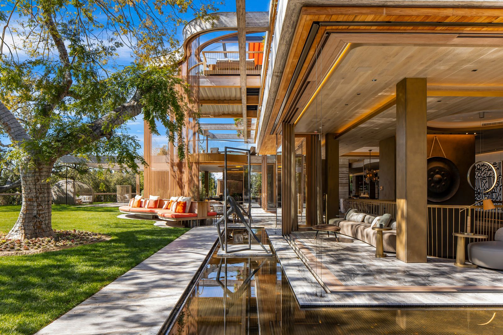 Covered terraces run directly beside the living spaces, while broad lawns extend beyond them beneath the trees.