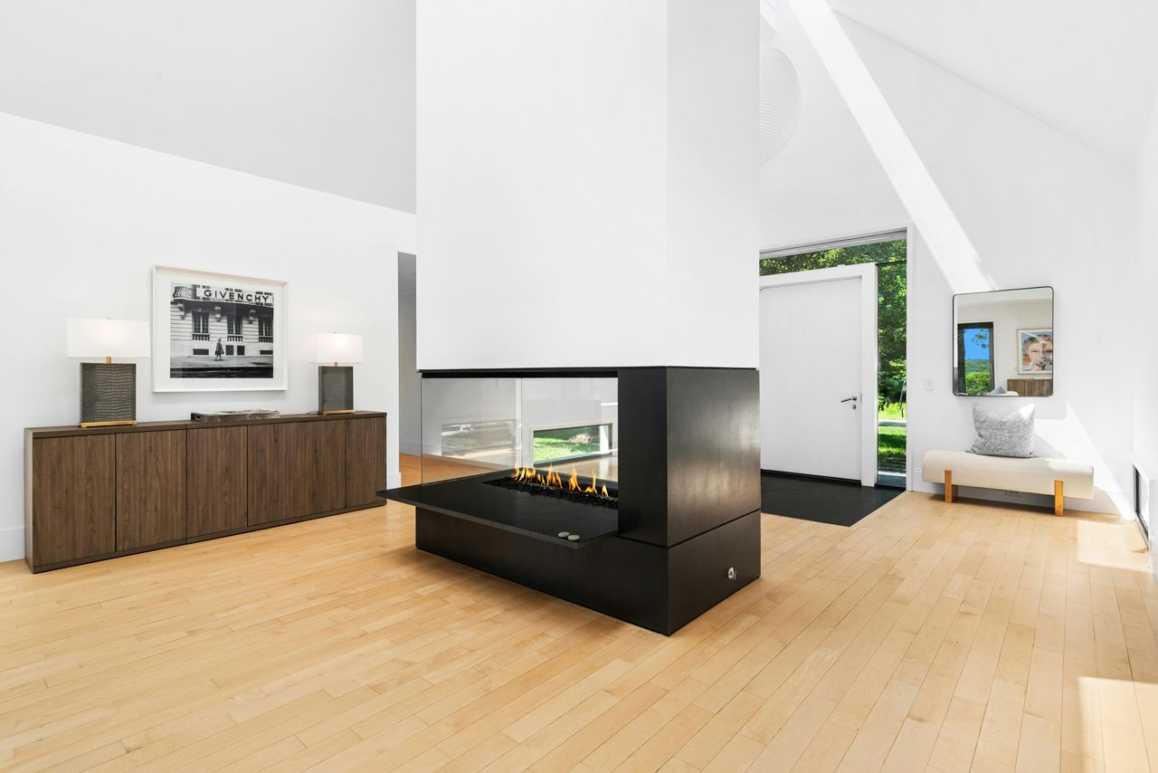 At the center, a large black-framed fireplace acts like a freestanding divider, with glass on multiple sides allowing the flames to be seen from different parts of the entry. 