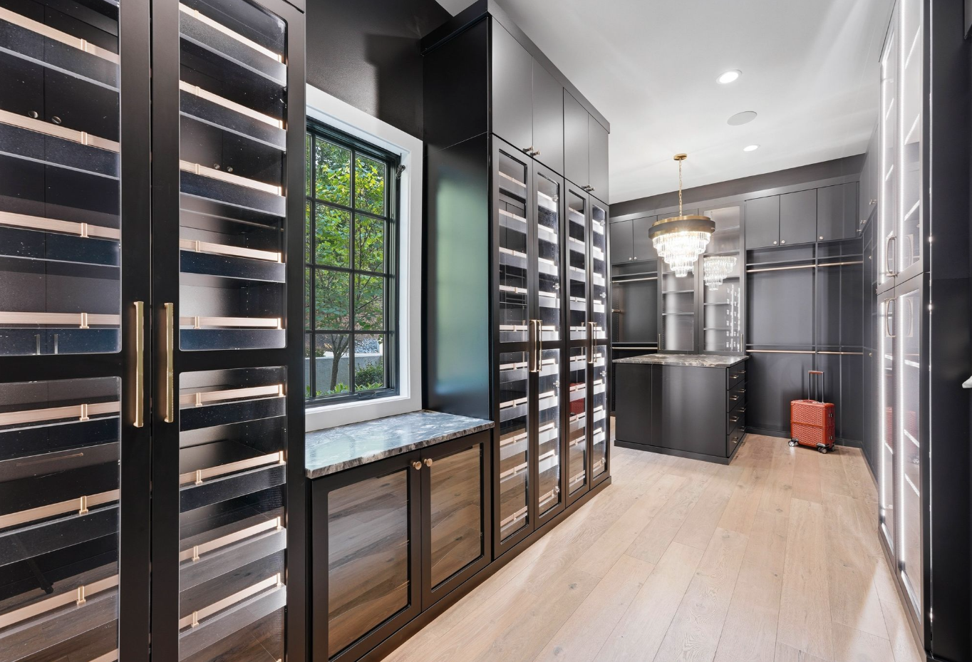 Dressing room with floor-to-ceiling black cabinetry, brass rails, integrated drawers, and stone-topped storage islands. 
