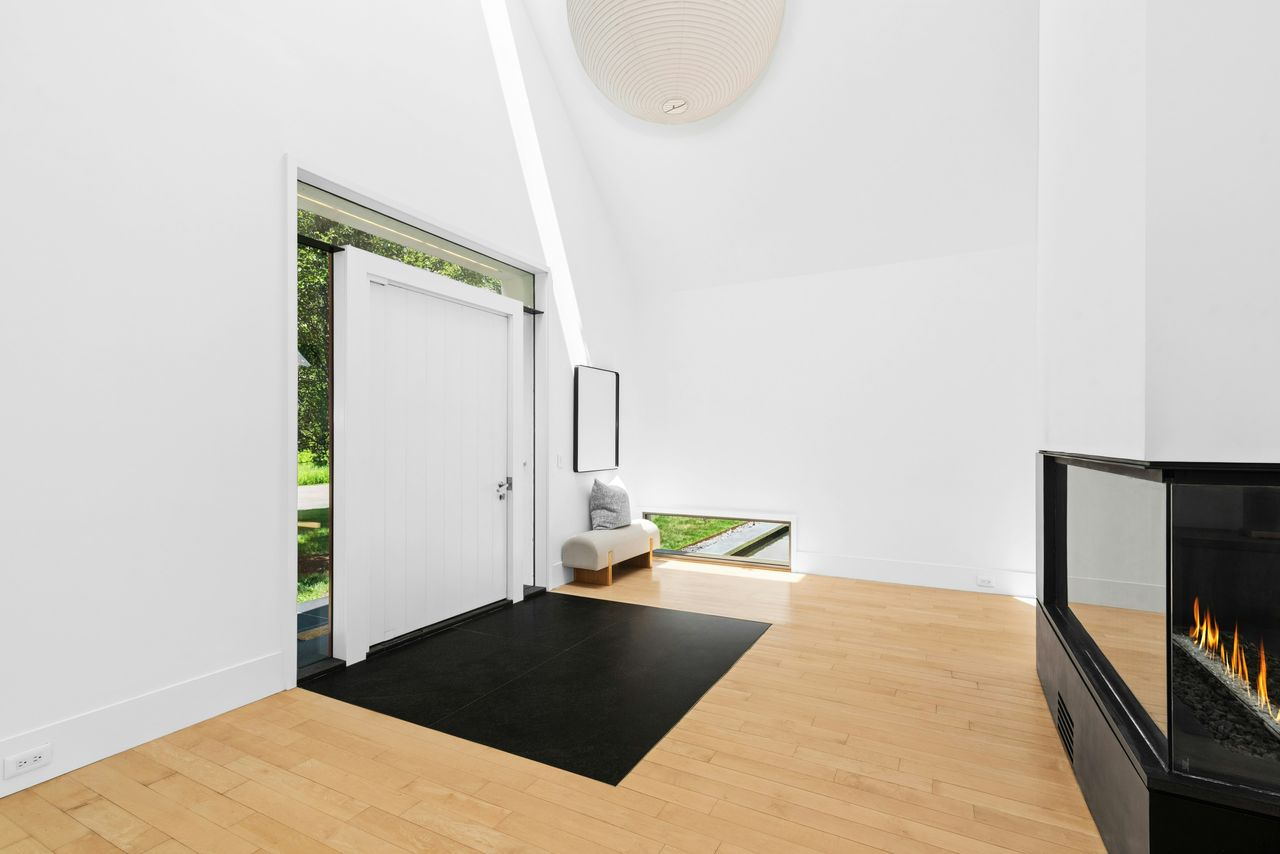 Stepping through the front door, the foyer opens into a tall, sharply angled room with white walls and pale wood floors, keeping the entrance bright and uncluttered.
