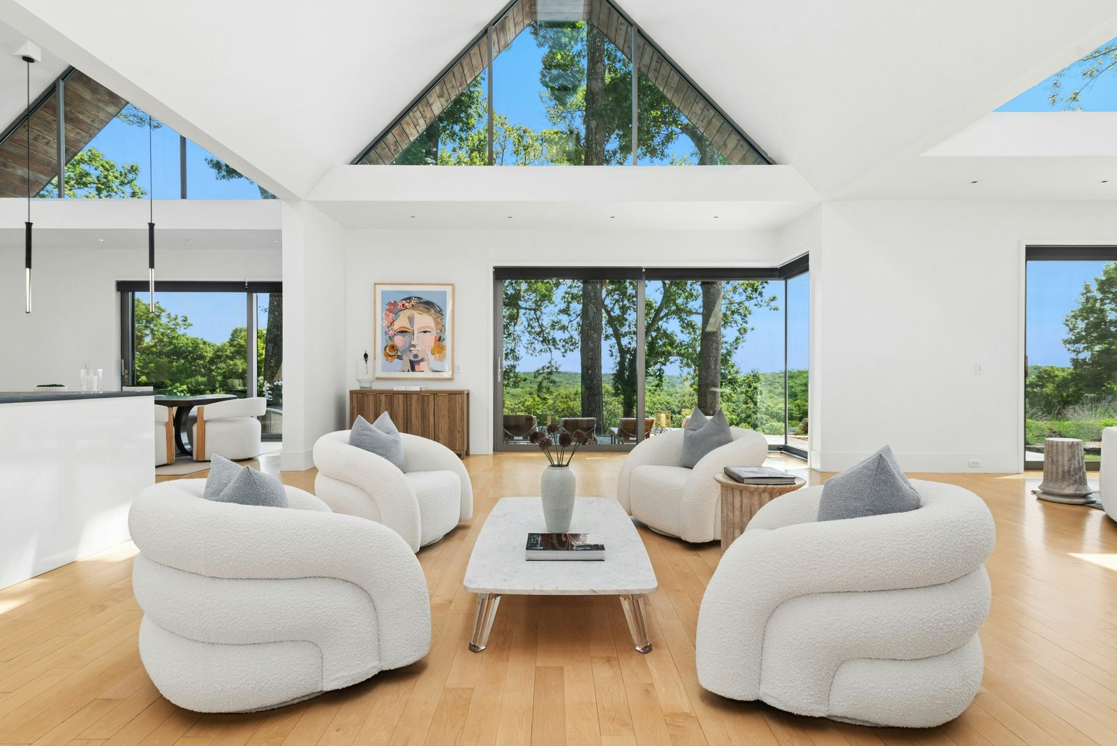 The first seating area sits directly in front of the largest glass wall, where four sculptural lounge chairs are arranged around a low rectangular coffee table. 