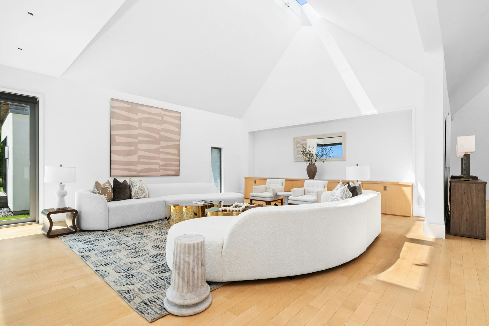 Curved white sofas wrap around a central grouping of gold tables, while additional lounge chairs are tucked along the back wall.