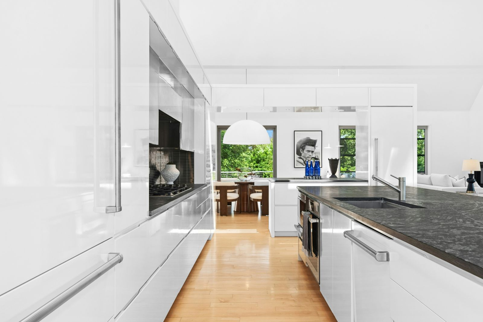 Glossy white cabinetry runs nearly floor to ceiling around the room, paired with stainless-steel appliances and a dark tile backsplash. 