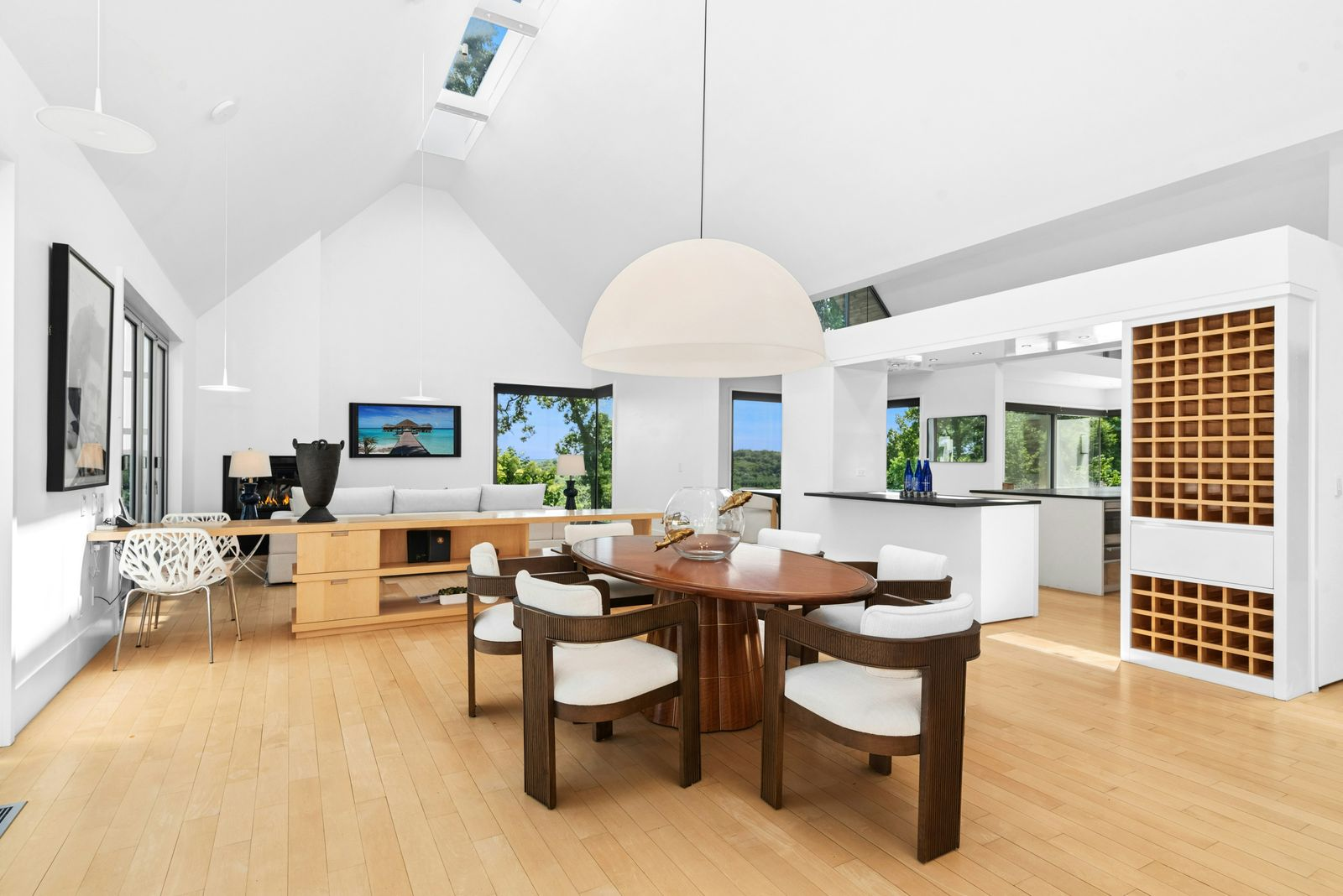 A round wood table sits at the center with six upholstered chairs, while an oversized dome pendant hangs low above it.