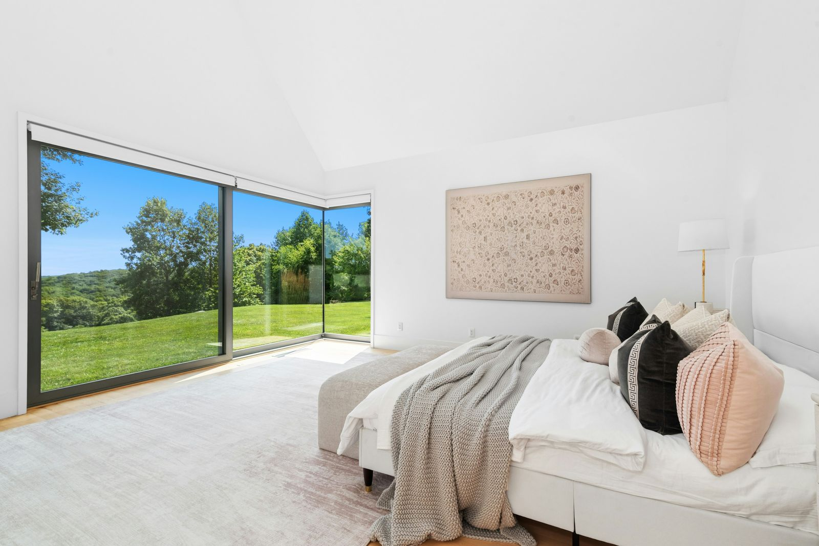 The bedroom opens toward full wall corner glass doors that frame the lawn and surrounding trees.
